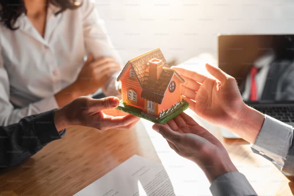 Two people holding a small model house during a property handover